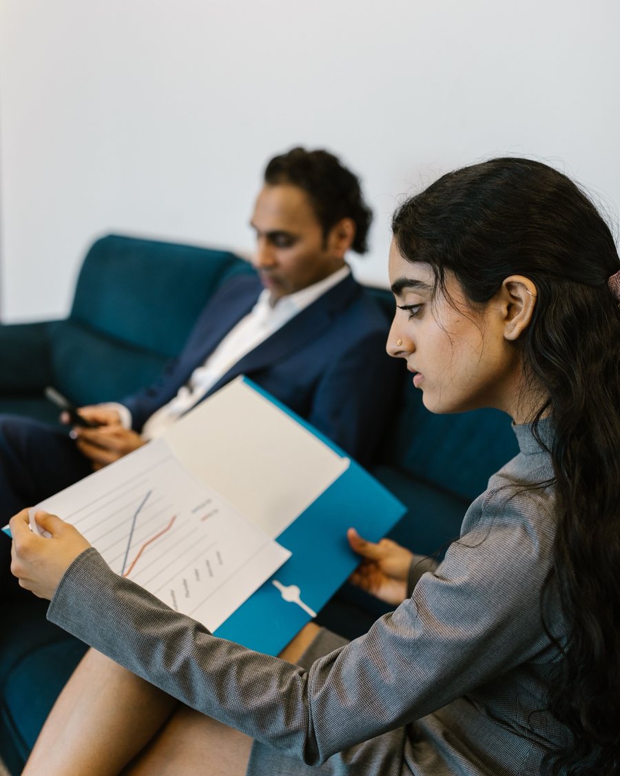 A young woman reviewing a chart in a folder while a colleague sits beside her