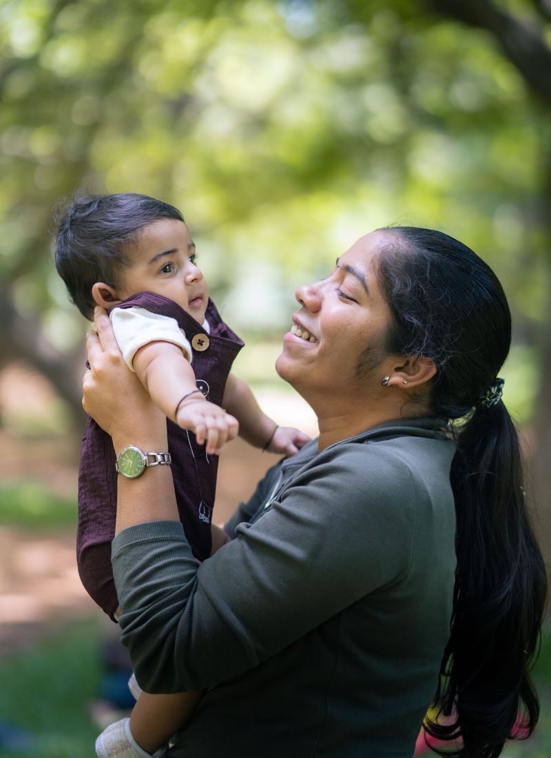A mother smiling as she holds her baby up outdoors